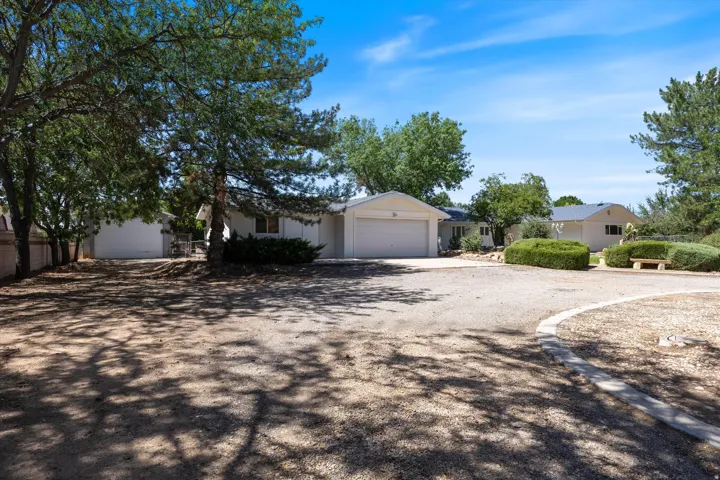 Gravel driveway with integrated curbing, mature trees, and a beige stucco exterior