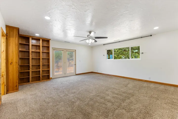Wall-to-wall carpeting, recessed lighting, built-in shelving, glass-paned double doors, and a ceiling fan