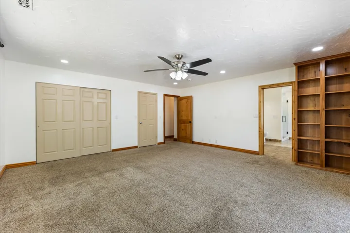 Spacious room featuring carpeting, a ceiling fan with light, recessed lighting, and built-in wood shelving