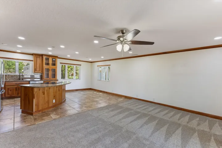 Open-concept living space featuring a kitchen with wood cabinetry, a curved island with a stone countertop, a tile backsplash, and a ceiling fan