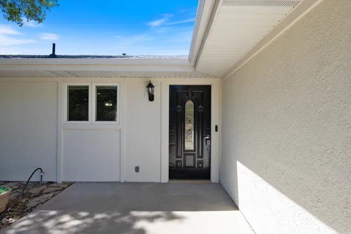 Stucco exterior with a covered entry, black paneled door with decorative glass inserts, and an exterior wall lantern