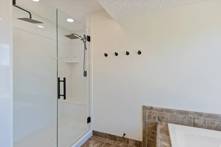 Glass-enclosed shower with matte black fixtures, dual showerheads, and integrated bench seating