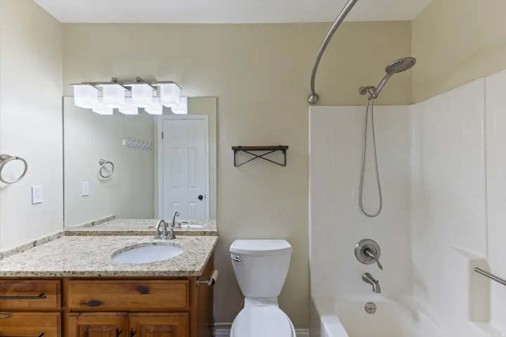 Bathroom featuring a wood-finish vanity with a light-toned granite countertop, undermount sink, and a large mirror