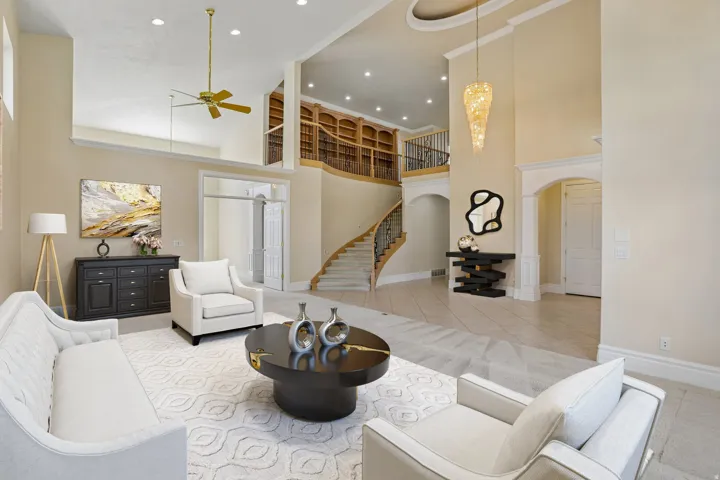 Two-story foyer with a grand curved staircase, built-in library shelving, tray ceiling, and an elegant chandelier