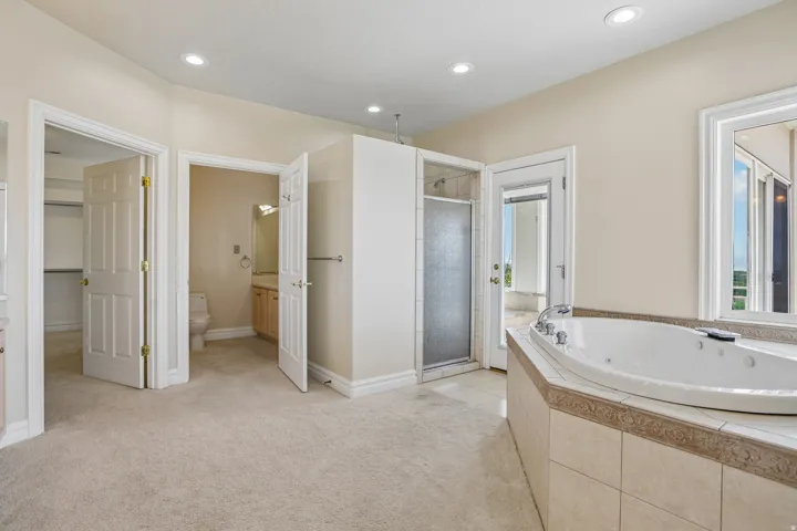 Soaking tub with tile surround, glass-enclosed shower, dual panel doors, recessed lighting, and a large window