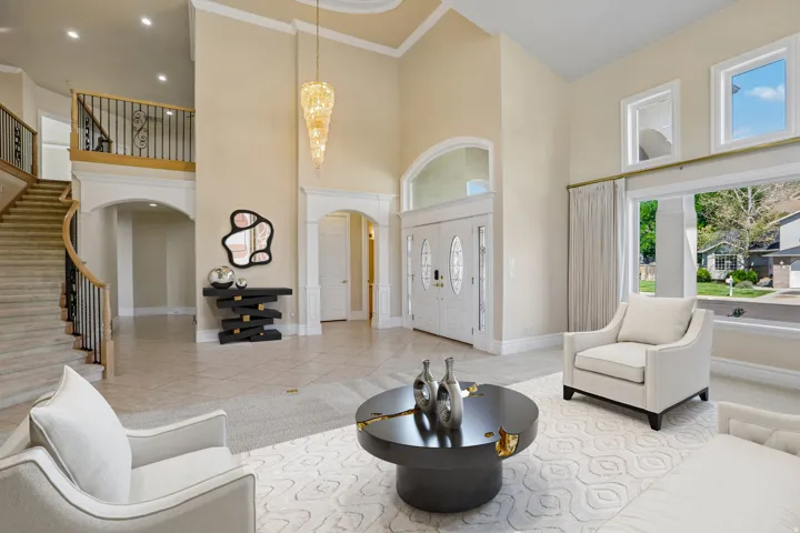 Two-story foyer with tile flooring, a grand curved staircase featuring wrought iron balusters, and double entry doors with decorative glass