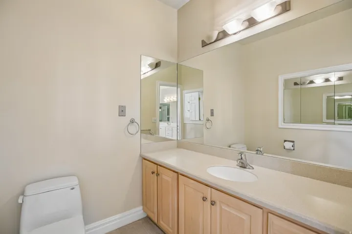 Extended vanity with an integrated sink, broad wall mirror, natural wood-finish cabinetry, and overhead bar lighting