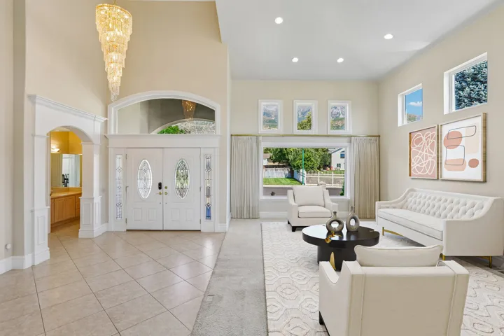 Vaulted ceilings with a tiered chandelier, tile flooring, double entry doors with decorative glass, and multiple windows providing natural light