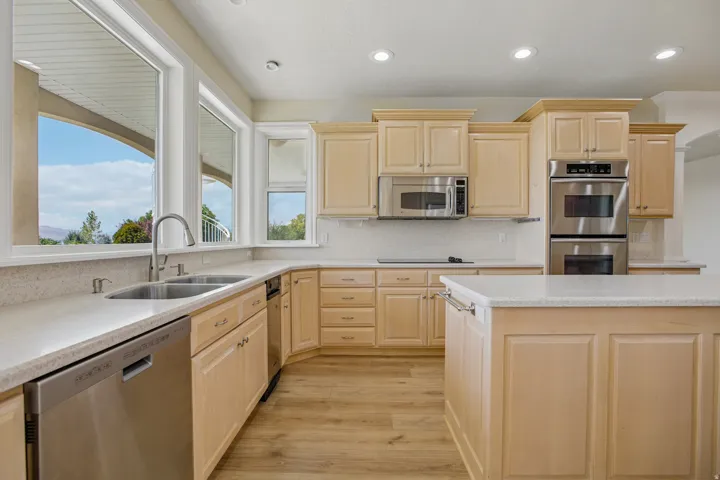 Contemporary kitchen featuring light wood cabinetry, stainless steel appliances, a center island, and wood-finish flooring