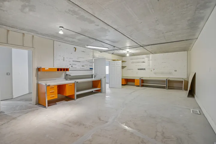 Expansive concrete flooring and exposed ceiling, featuring multiple built-in workstations and pegboard walls
