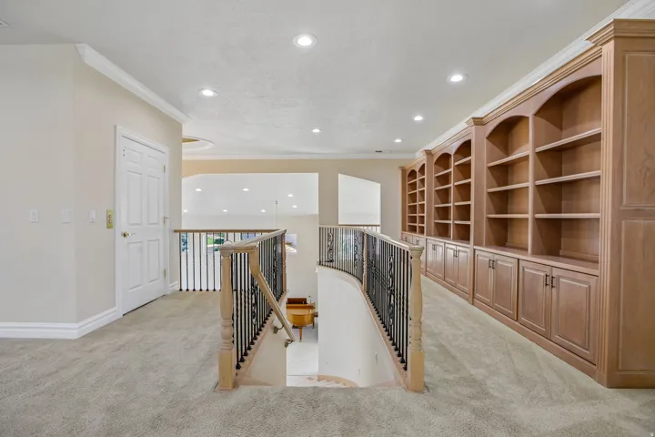 Built-in wood cabinetry with arched shelving, recessed ceiling lighting, and a curved staircase with wrought iron railing
