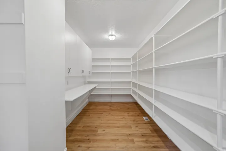 Extensive built-in shelving, white cabinetry with silver hardware, integrated counter space, wood-finish flooring, and overhead lighting