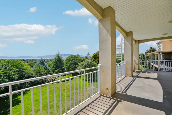 Spacious covered balcony with concrete flooring, white railings, and a spiral staircase