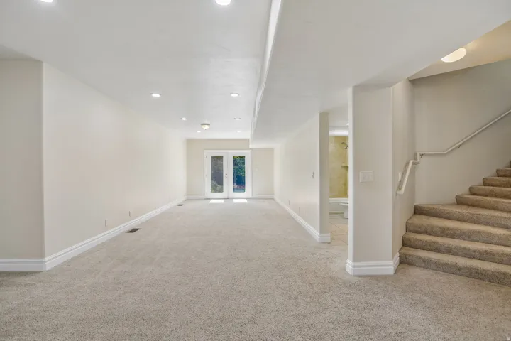 Expansive carpeted area with recessed lighting, white trim, and a double glass-paned door