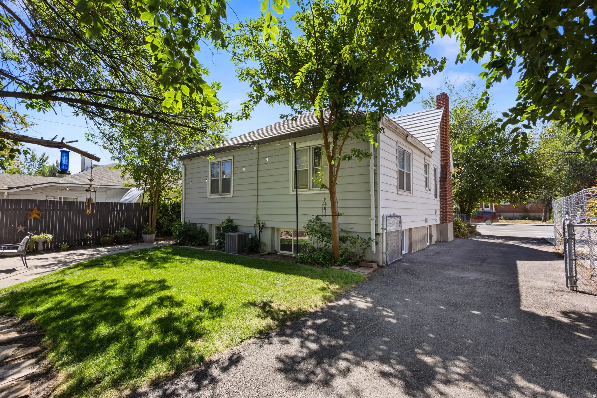 Expansive lawn area, paved driveway, mature trees, wood privacy fence, and brick chimney
