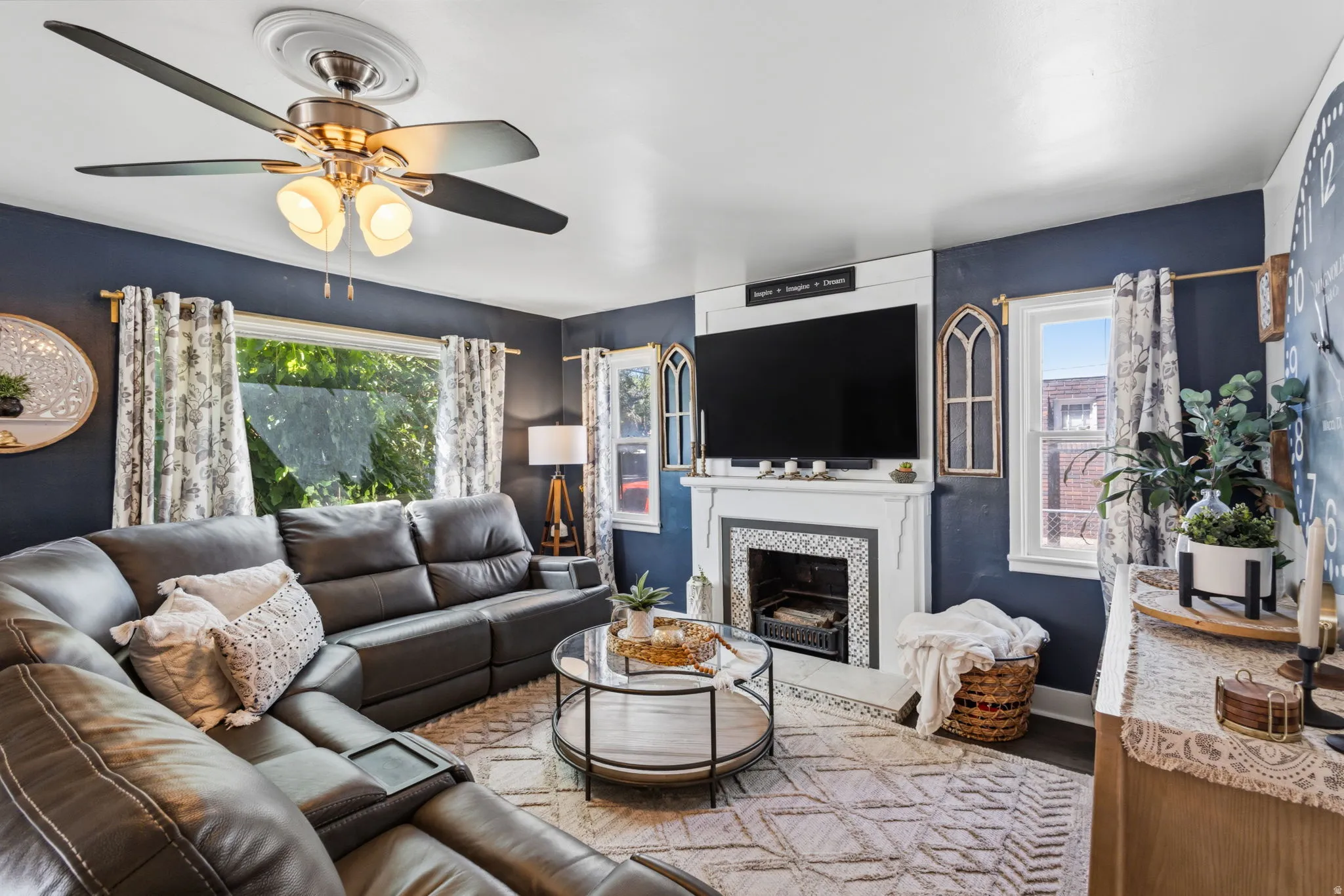 Ceiling fan with integrated lighting, built-in fireplace with tile surround, white trim window frames, and hard surface flooring