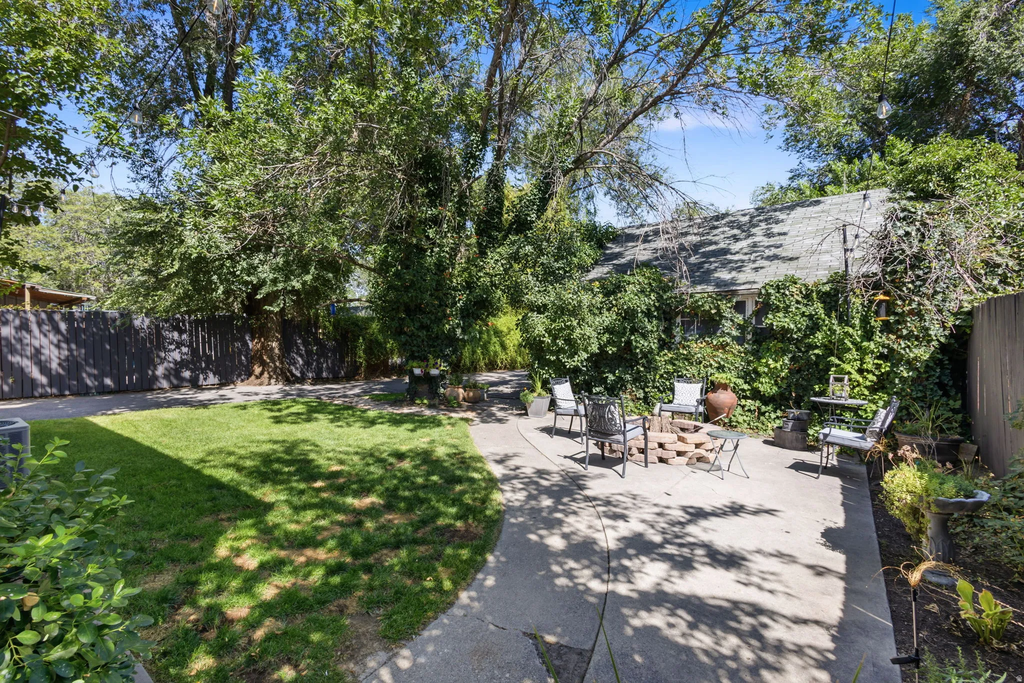 Expansive backyard featuring a manicured lawn, concrete patio, a privacy fence, and mature trees