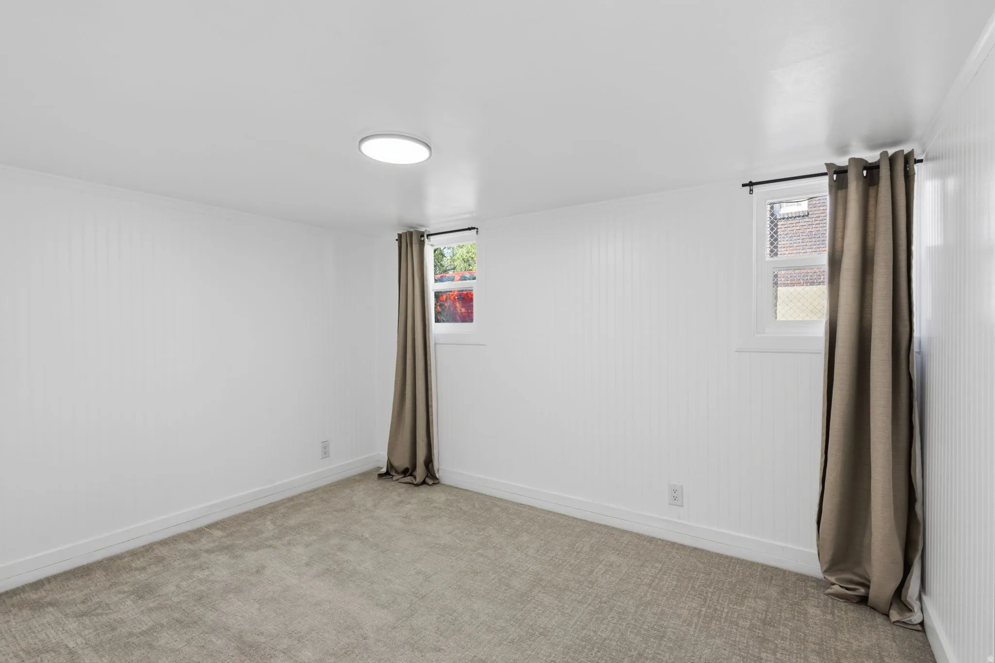 White vertical paneling on walls, light-colored carpeted flooring, overhead flush-mount lighting, and two windows