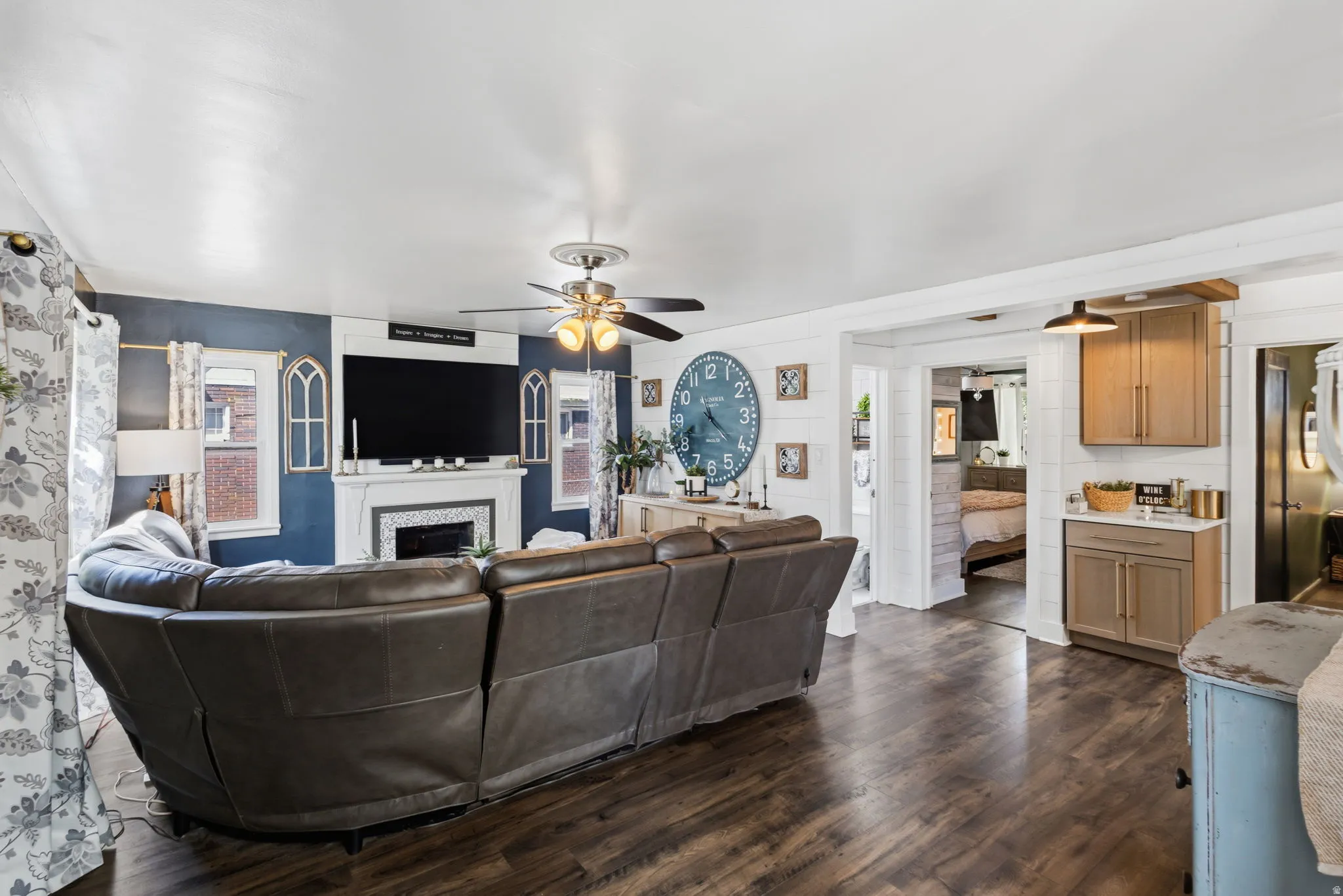Wood-finish flooring throughout, featuring a built-in fireplace with a white mantel and tile surround, and an integrated ceiling fan