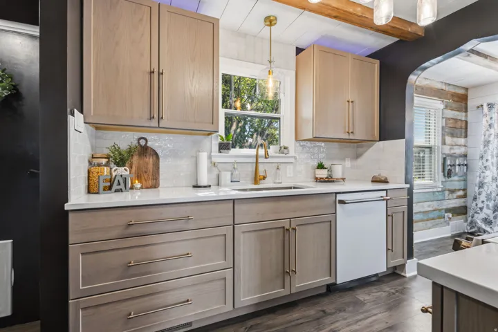 Kitchen featuring light wood-tone cabinetry, white countertops, mosaic tile backsplash, and a gold-finish gooseneck faucet