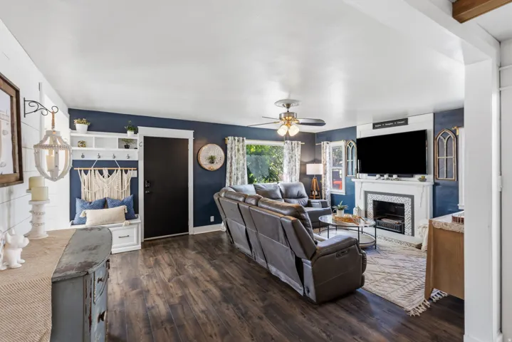 Wood-finish flooring throughout, built-in mudroom bench with storage, fireplace with decorative tile surround, ceiling fan, and built-in shelving