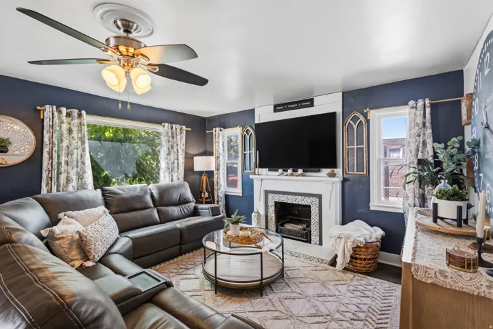Ceiling fan with integrated lighting, built-in fireplace with tile surround, white trim window frames, and hard surface flooring