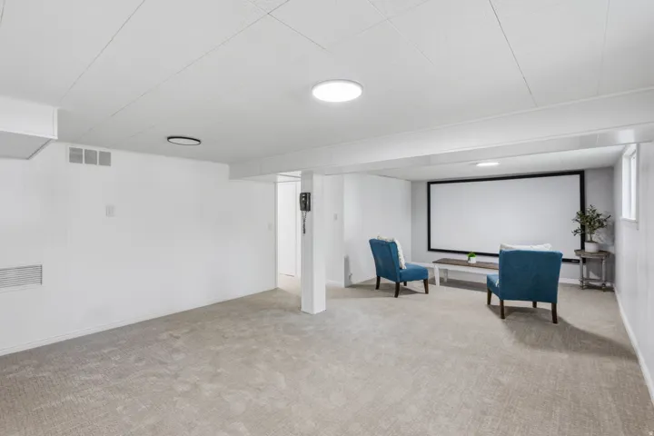 Expansive open-concept room featuring a large projection screen, recessed lighting, and soft carpet flooring