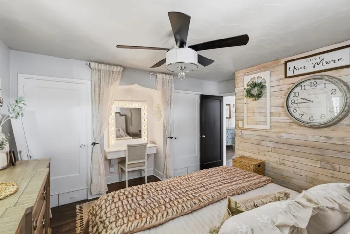 Textured wall paneling, ceiling fan with integrated lighting, wood-finish flooring, and a built-in vanity with illuminated mirror