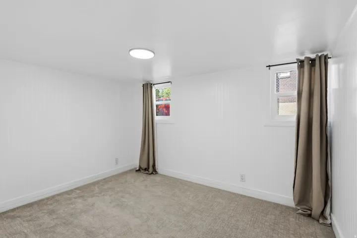 White vertical paneling on walls, light-colored carpeted flooring, overhead flush-mount lighting, and two windows