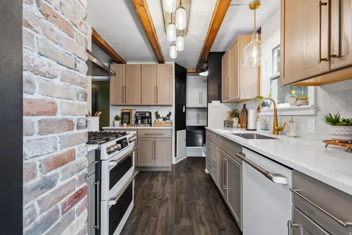 Exposed brick accent wall, wood-finish flooring, white countertops, dual-tone cabinetry, and a gold-finish faucet