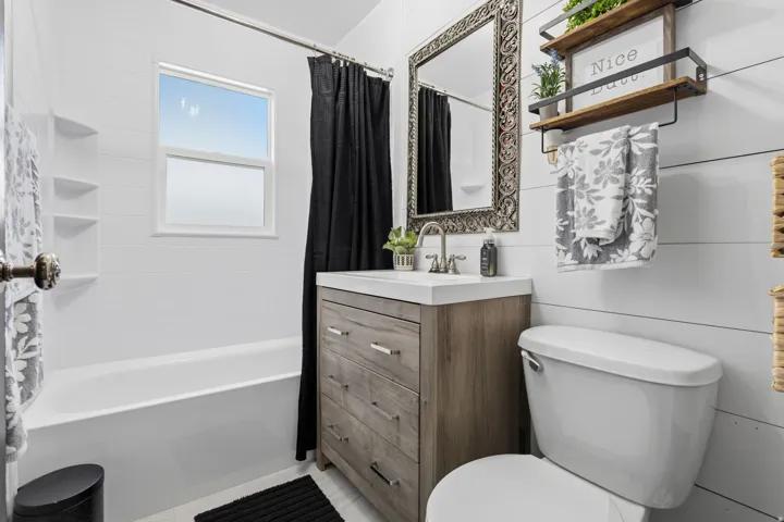 Bathroom featuring a window, white tile shower surround, wood-finish vanity with an integrated sink, and an ornate framed mirror