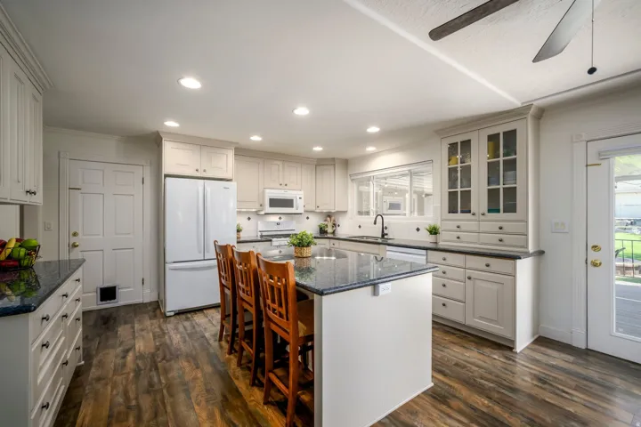 Kitchen featuring wood-finish flooring, recessed lighting, beautiful cabinetry, a central island with a dark countertop, and a glass-paneled door leading outdoors
