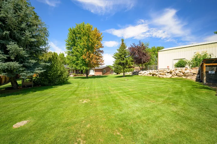 Expansive grass lawn featuring mature trees and a rock wall retaining feature