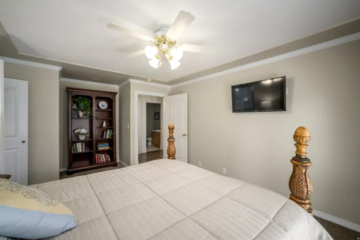 Tray ceiling with crown molding, ceiling fan with integrated lighting, wall-mounted television, and wood-finish door