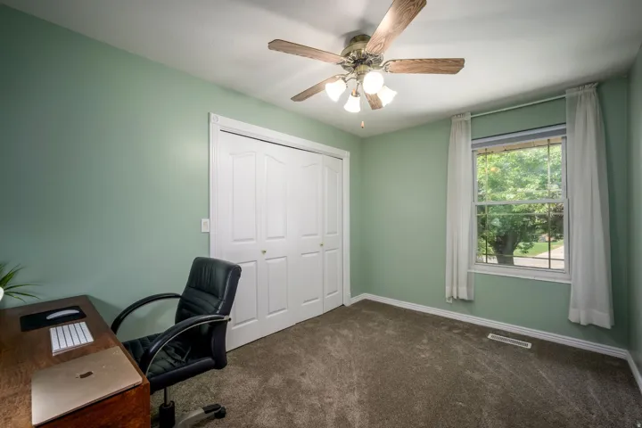 Carpeted room featuring a ceiling fan with light fixture, bifold closet doors, and a window providing natural light