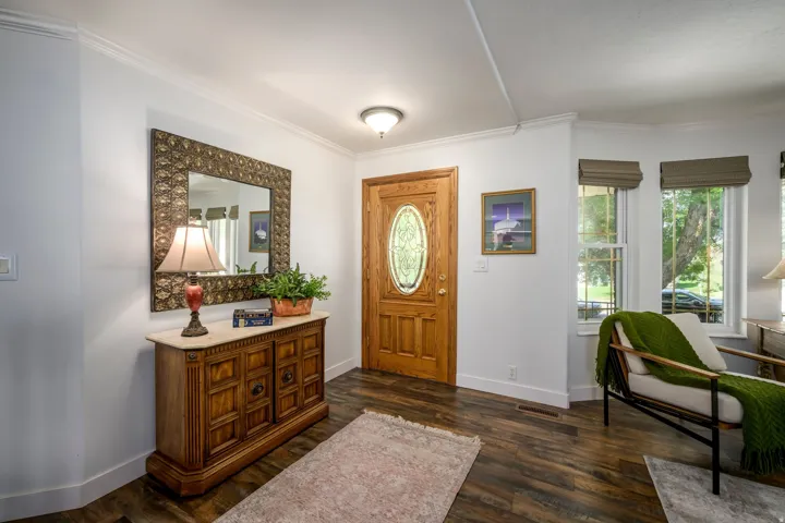 Rich wood-finish flooring, white molding, and a solid wood entry door with oval glass insert