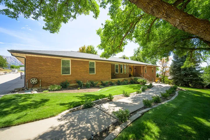 Brick exterior with a dark-pitched roof, featuring a concrete pathway framed by manicured landscaping, and expansive green lawn areas