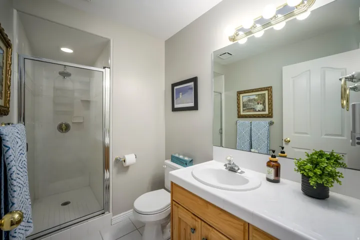 Glass-enclosed shower with a recessed light, wood-finish vanity with a white countertop, and a large wall-mounted mirror with integrated lighting