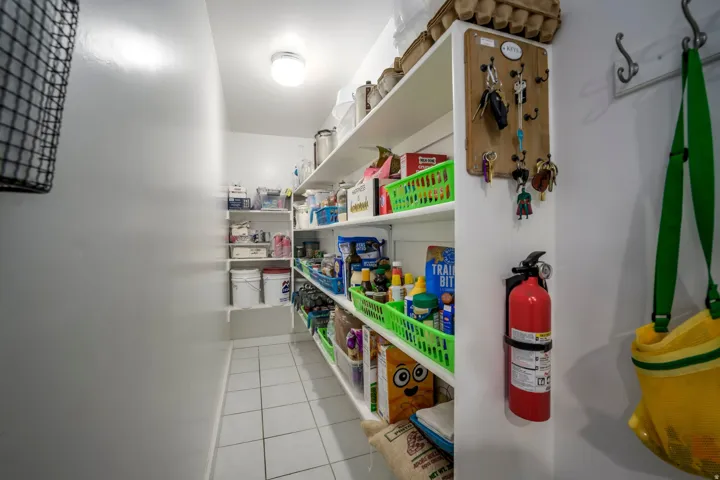 Spacious pantry with white shelving, white tile flooring, and overhead flush mount lighting