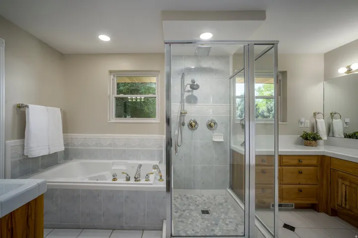 Built-in jetted tub, glass-enclosed shower with tile surround,  vanity with wood-finish cabinetry