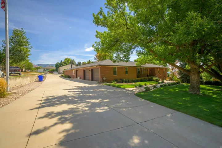 Brick exterior residence with a concrete driveway, attached garage, manicured lawn, and mature trees