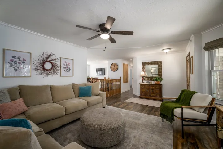 Spacious living area featuring wood-finish flooring, a ceiling fan, and molding