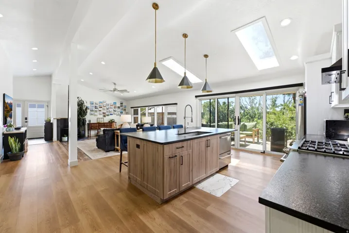 Vaulted ceiling with skylights, wood-finish flooring, kitchen island with integrated sink, stainless steel appliances, and sliding glass doors to outdoor deck