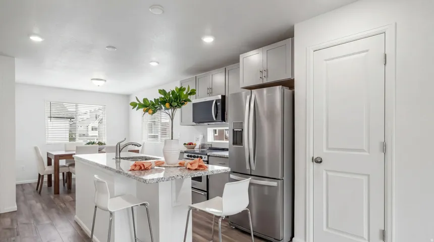 Kitchen featuring a central island with a sink, stainless steel appliances, light gray cabinetry, and wood-finish flooring