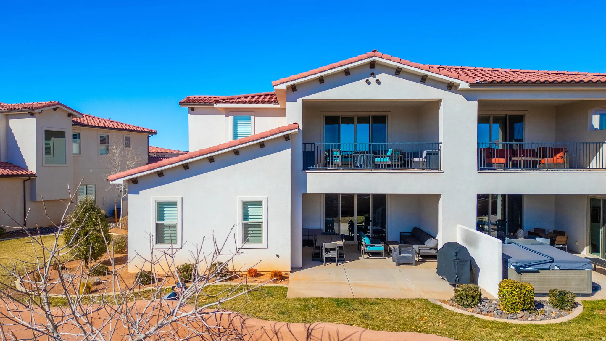 Stucco exterior with a red tile roof, featuring covered balcony with black railings, and a ground-level patio