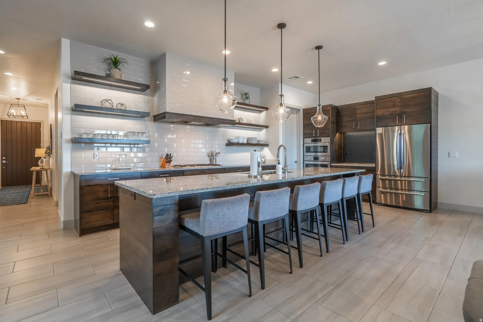 Kitchen featuring a large island with stone countertops, built-in stainless steel appliances, dark wood-finish cabinetry, a subway tile backsplash, and wood-look flooring