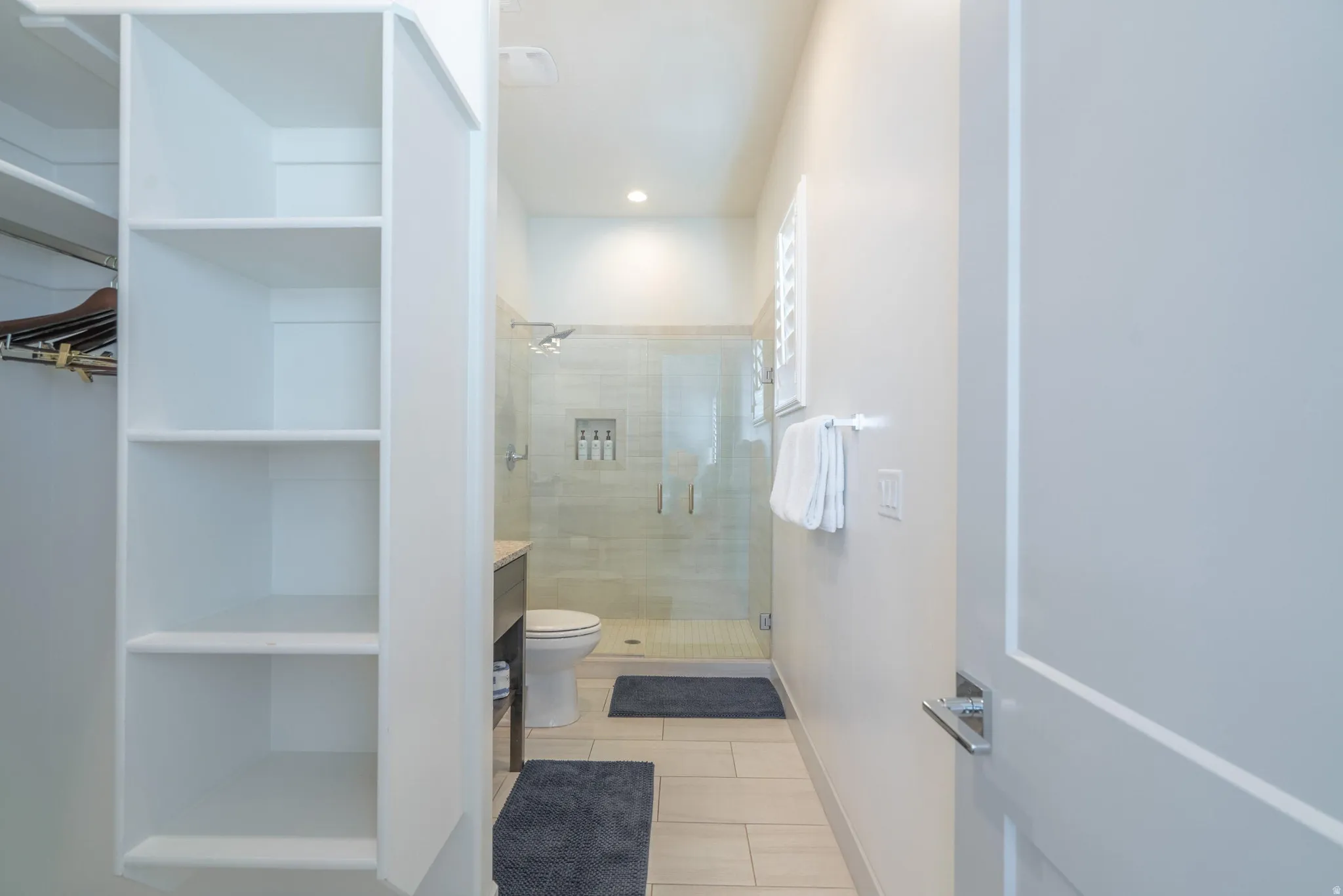 Main Floor Bedroom 2 Ensuite with Built-in shelving and closet rod, walk-in shower with glass enclosure, recessed shower niche, and louvered window