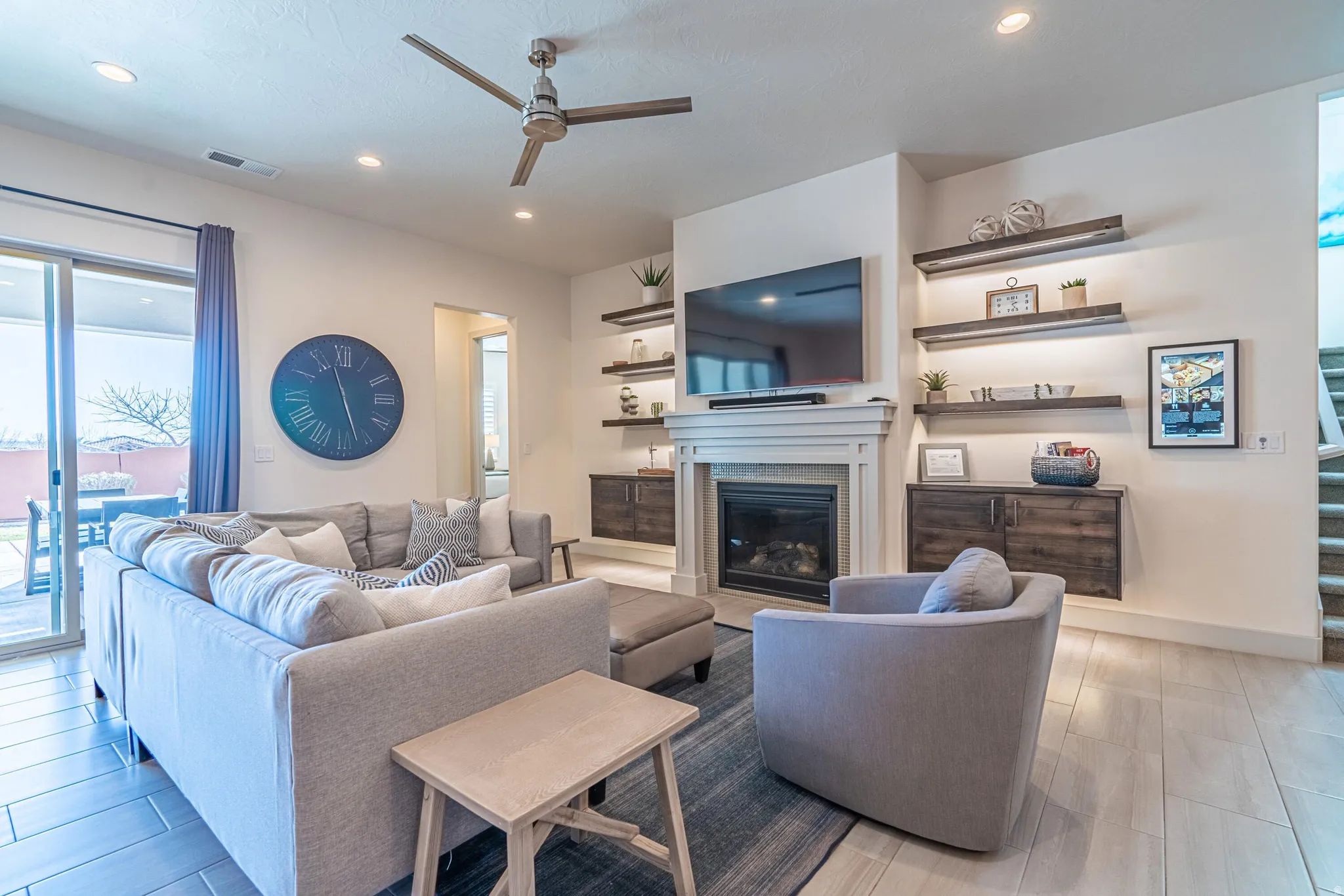 Recessed lighting, ceiling fan, fireplace with mantel, built-in shelving with under-shelf lighting, and wood-finish flooring