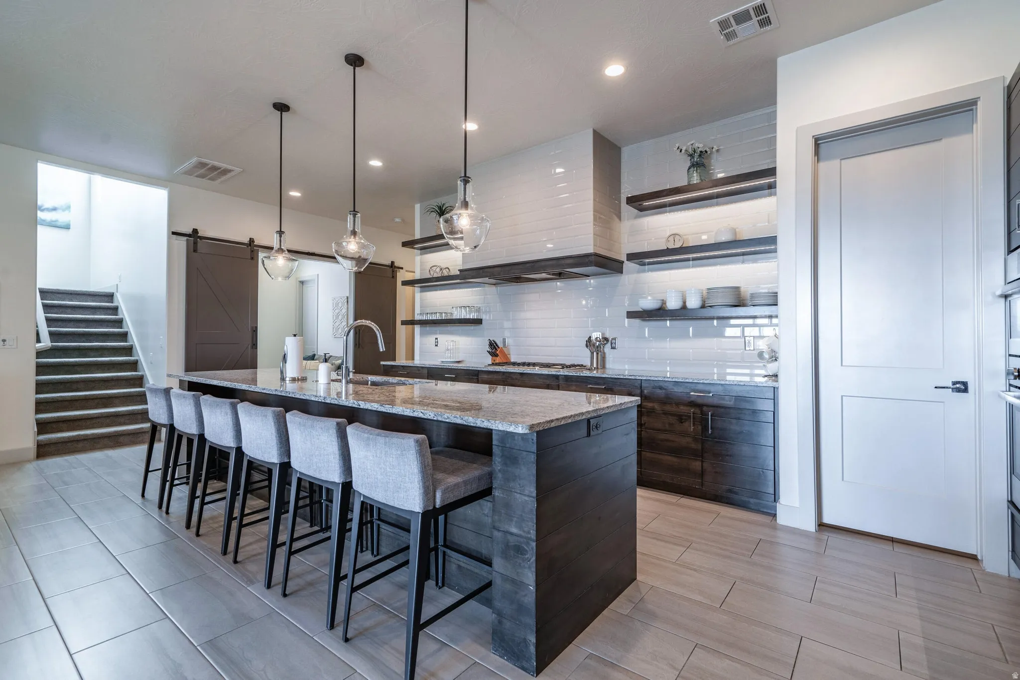 Gourmet kitchen featuring a large island with seating, a professional-grade range hood, open shelving, and integrated appliances