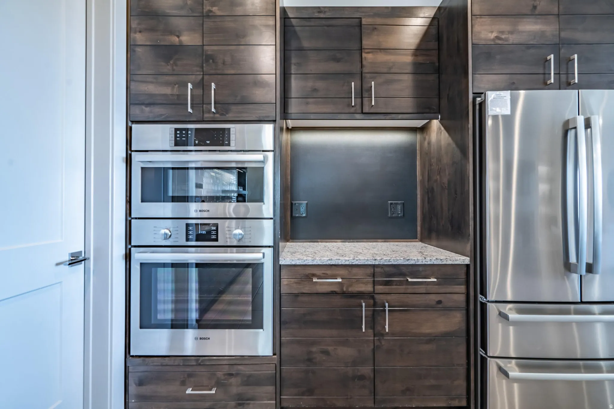 Built-in stainless steel appliances, dark wood-finish cabinetry, under-cabinet lighting, and a granite countertop